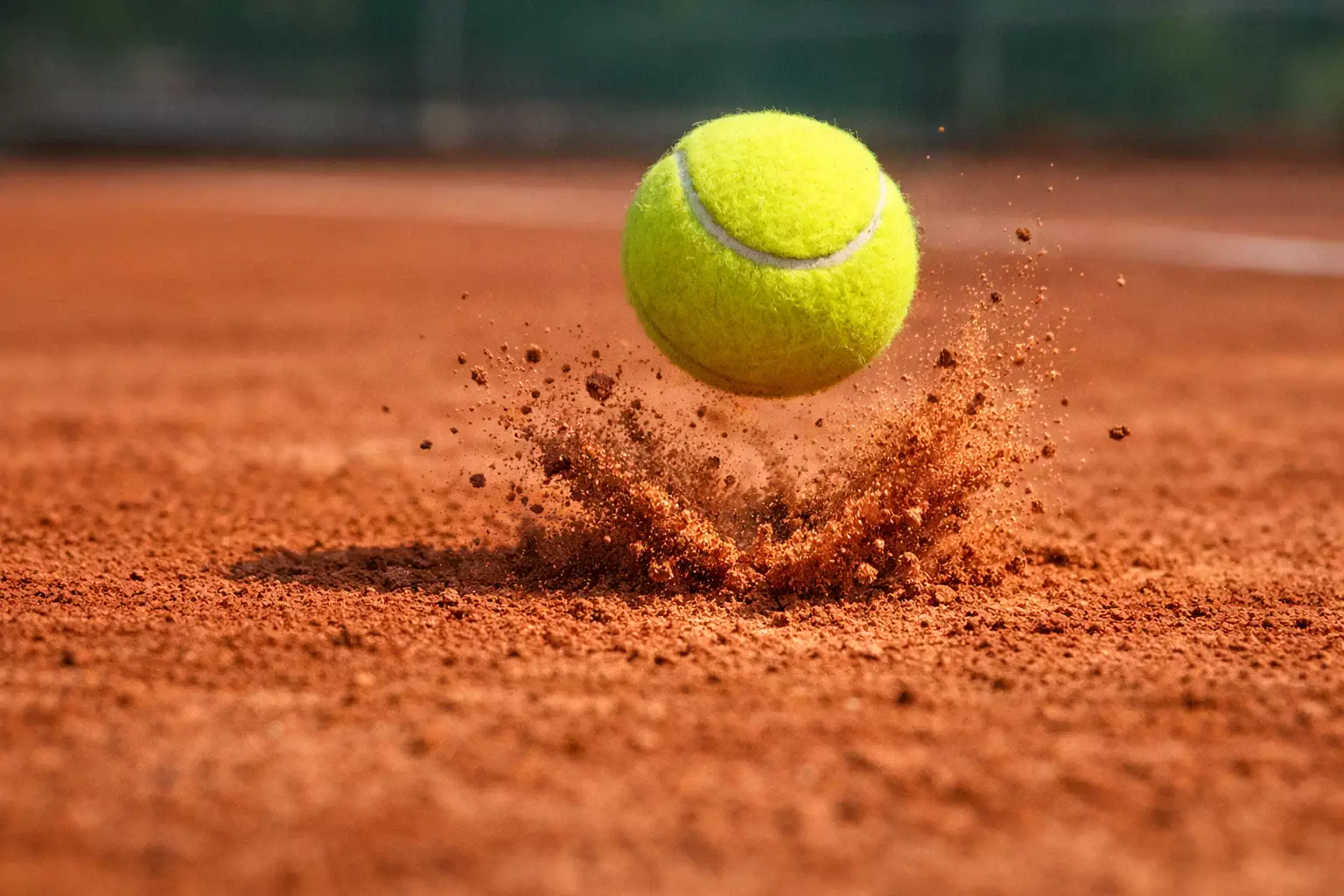 Pelota de tenis amarilla rebotando sobre pista de arcilla roja