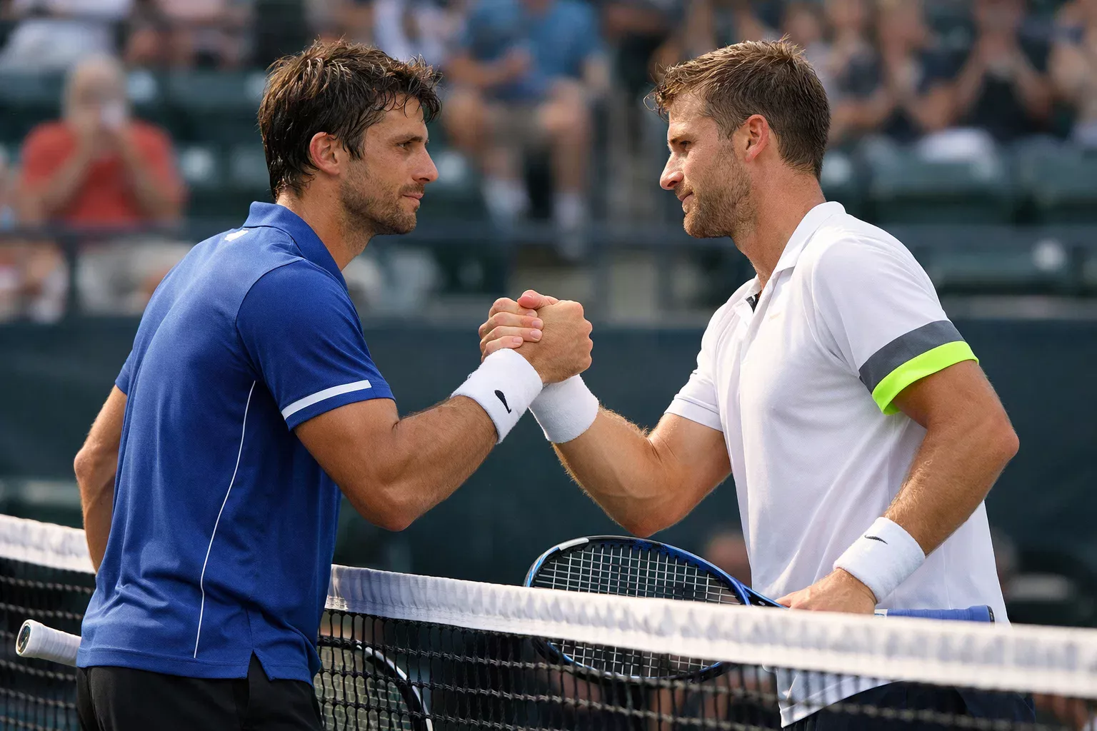 Dos tenistas profesionales estrechando manos en la red tras partido