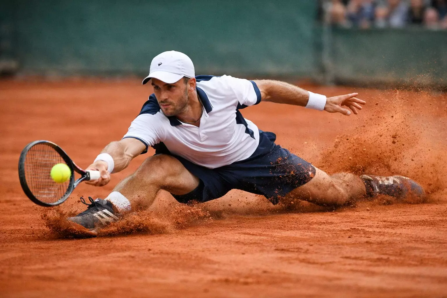 Tenista deslizándose sobre tierra batida para alcanzar la pelota
